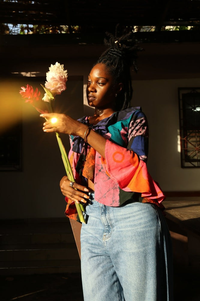 Colorful Pastiche Clo top with eclectic patterns, paired with denim, complemented by a bouquet of flowers.