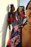 Four women on balcony in Pastiche Clo attire, basking in sunlight, showcasing colorful patterns and sustainable style.