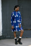 Model in Press Dress in Location batik print, long sleeves, and knee-length hem, paired with white socks and black boots.