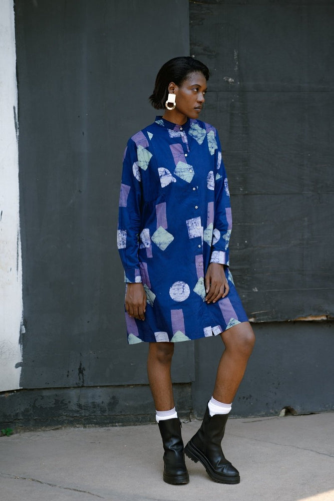 Model in Press Dress in Location batik print, long sleeves, and knee-length hem, paired with white socks and black boots.