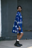 Side view of model in oversized Press Dress with white circular patterns, black shorts, white socks, and black shoes.