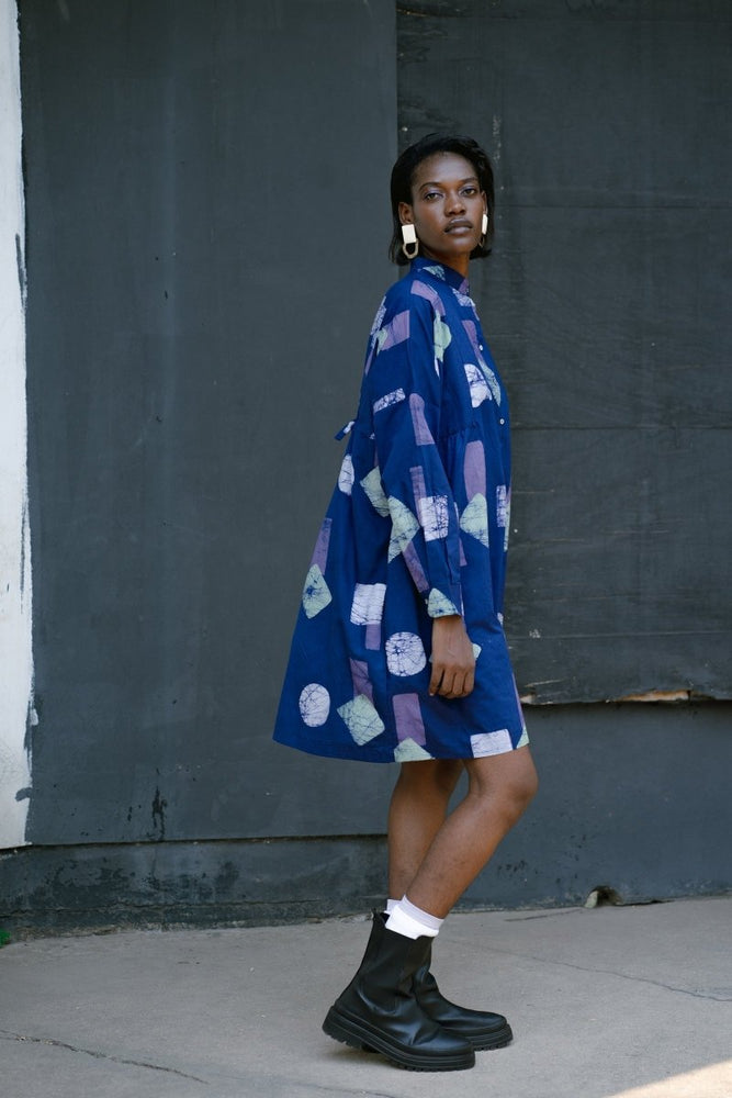 Side view of model in oversized Press Dress with white circular patterns, black shorts, white socks, and black shoes.