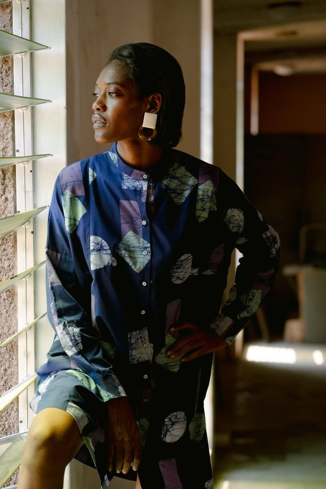 Woman stands next to window wearing the Press Dress in the Location hand-dyed batik print.