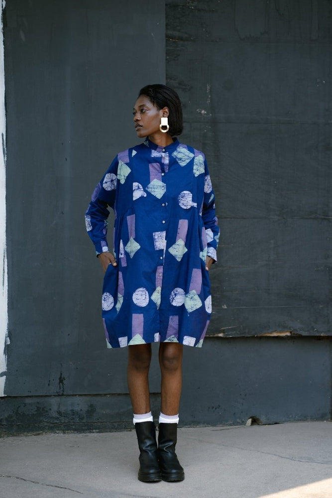 Model in blue batik print dress with circular patterns, long sleeves, and knee-length hem, paired with white socks and black boots.