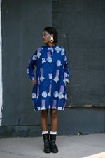 Model in blue batik print dress with circular patterns, long sleeves, and knee-length hem, paired with white socks and black boots.