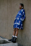 Model in the Press Dress in Location print with white circular patterns, black boots, and white socks, standing against a wall.