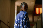 Back view of model in Press Dress with white rectangular patterns, standing in a dimly lit indoor space with warm light.