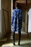 Back view of model in Press Dress with white patterns and black boots, standing in a corridor with natural light.