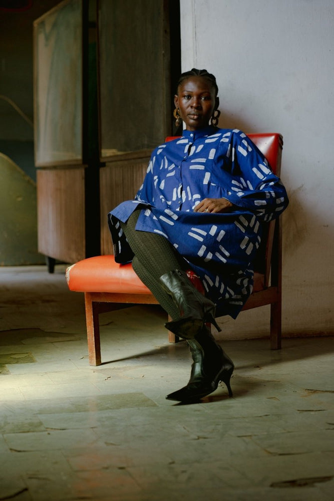 Model is seated in the Press Dress with Middle Path batik print, showcasing long sleeves, mandarin collar.