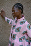 Side view of a model in a loose-fitting, long-sleeved Press Dress with mandarin collar and batik print, hand-sewn in Ghana, against a textured wall.