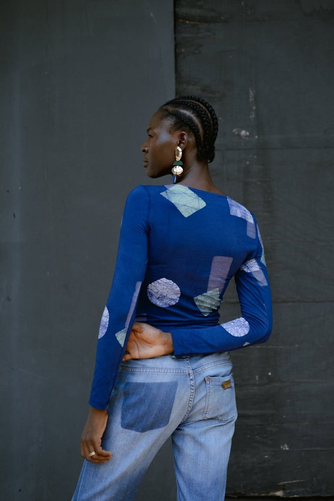 Model in Rift Top with Location print and blue jeans, showcasing the long sleeves and geometric pattern.