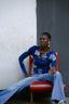 Model in Rift Top with Location print and blue jeans, seated on a red chair against a white wall.