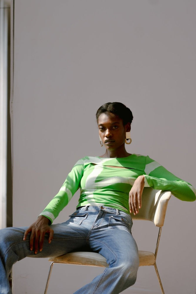 Model in Rift Top with the green with white waves Mangrove print, seated on a white chair. 