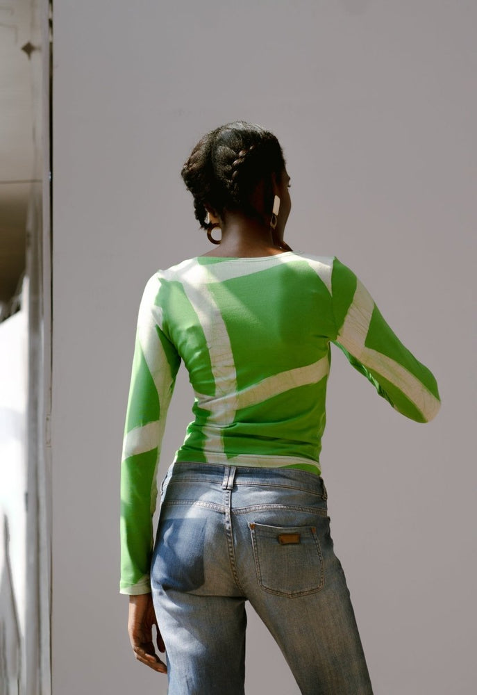 Back view of a person wearing the Rift Top in Mangrove print and blue jeans, standing against a natural light background.