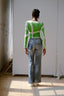 Back view of a person wearing the Rift Top in Mangrove print and blue jeans, standing in a naturally lit indoor setting.