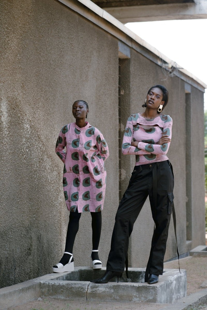 Two models on steps, both wearing the unique pink and green print design, one in the Press dress, the other in the Rift Top.