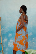 Saya Dress in orange and blue All Ideas print against a cloudy sky backdrop, exuding a dreamy aesthetic.
