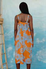 Model viewed from the back in Saya Dress with orange and blue abstract pattern, standing against a light blue backdrop.