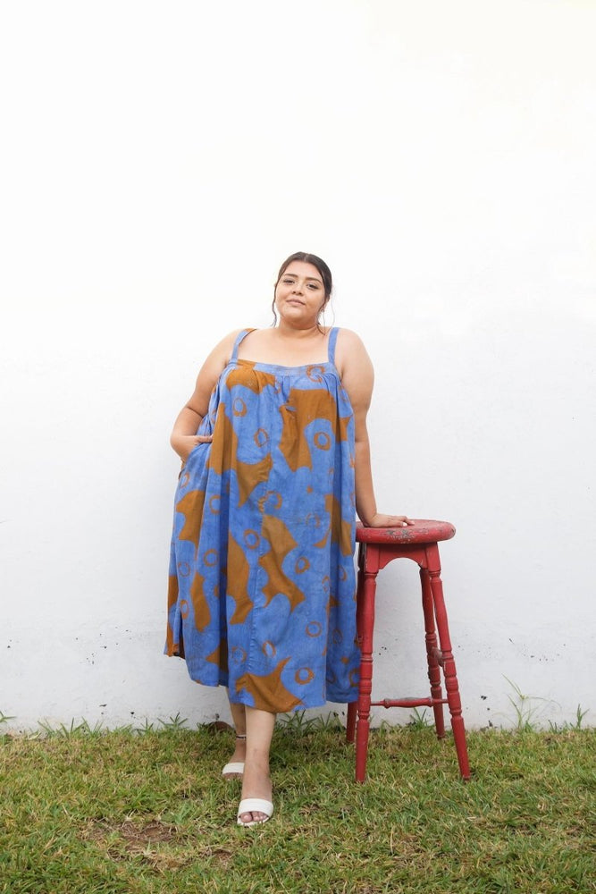 Graceful Saya Dress in All Ideas print, blue with orange floral patterns, against a white wall on grassy ground.