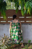 Back view of model in the Saya Dress in Waters, standing against a wall with rectangular cut-outs, surrounded by greenery.