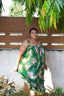 Full-length view of the Saya Dress in Waters print, standing outdoors against a brown wall with green foliage.