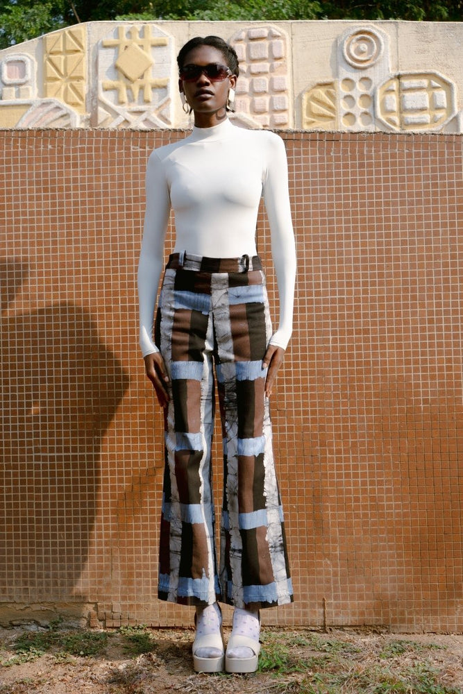 Veronica Trousers in Highlands batik print, worn with a white long-sleeved top against a tile wall.