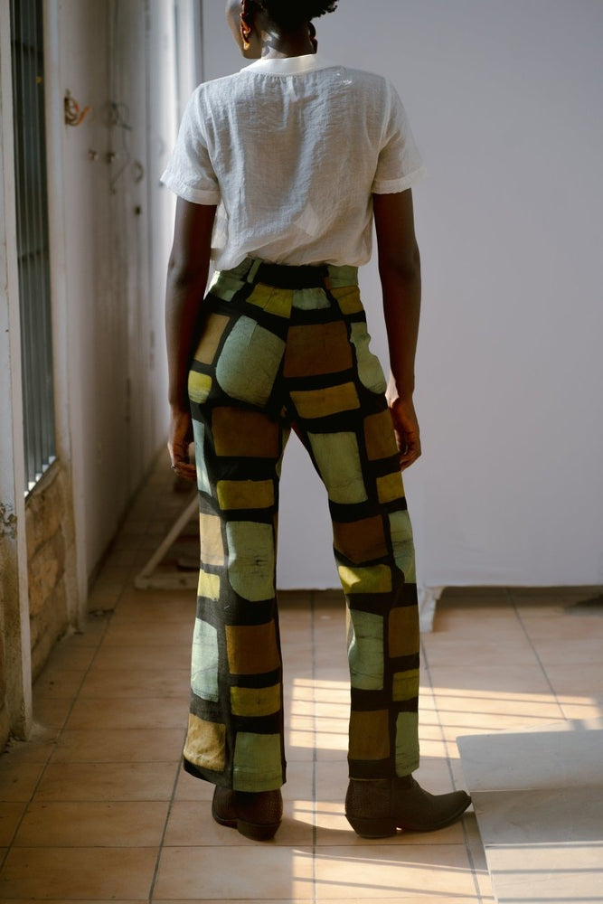 Back view of Veronica Trousers in Pistacia batik print, worn with a white t-shirt, standing in a sunlit room.