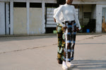 Veronica Trousers in Pistacia batik print, worn with a white top standing in front of garage-style doors.