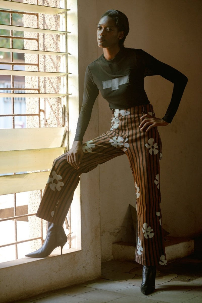 Person wearing Veronica Trousers in Ruga batik print with high-waisted flared design, standing by a window.