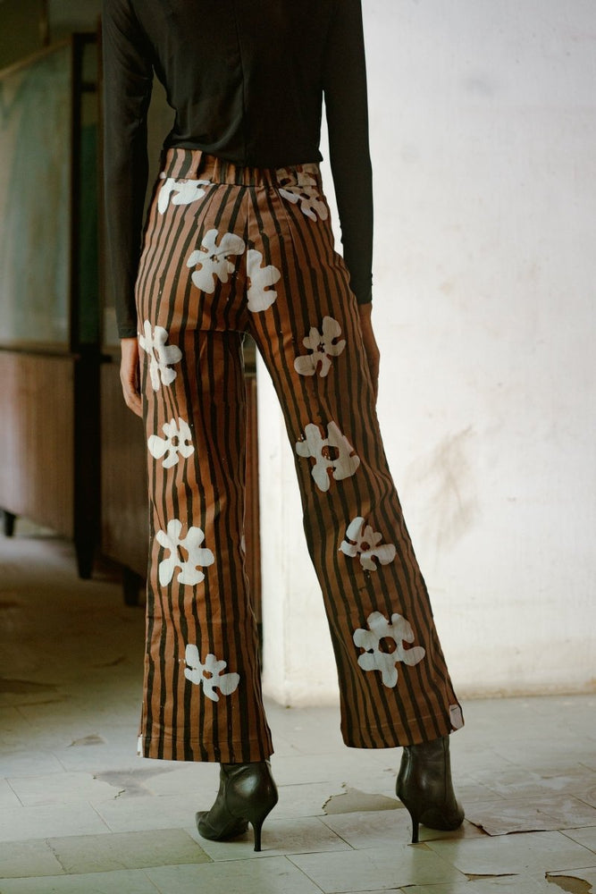 Back view of model wearing Veronica Trousers in Ruga batik print with black shoes, standing indoors on a tiled floor.