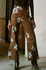 Model wearing Veronica Trousers in Ruga batik print with black boots and a black top, showcasing floral and striped patterns.