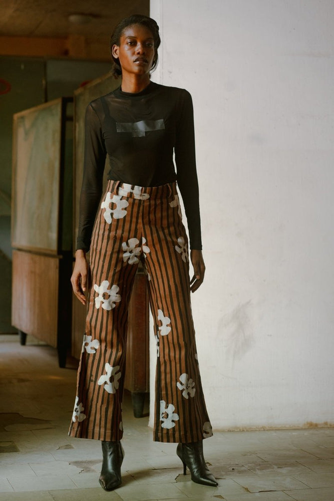 Model wearing Veronica Trousers in Ruga batik print with black boots and a long-sleeve black top, standing indoors.