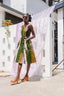 Colorful striped Amplo Dress in outdoor setting, paired with brown sandals, next to patterned hanging fabric.