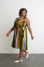 Amplo Dress in patchwork stripes of green, yellow, purple, cinched waist with sash, and white pointed heels.