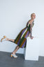 Amplo Dress in Speedboat stripes, model is casually leaning on pedestal, showcasing tattoos and white clogs.