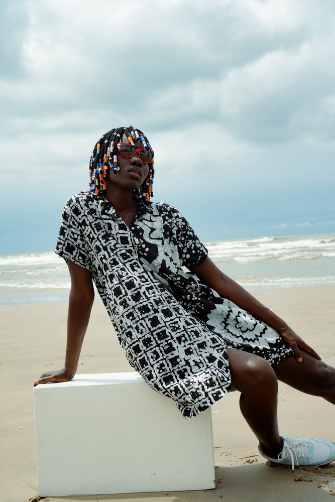 A woman in a relaxed pose wearing a black and white abstract flower and grid patterned oversized cotton dress in size small.