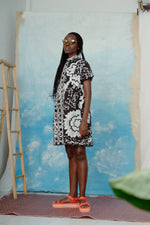 Side view of a woman wearing an oversized cotton dress in size small with a black and white abstract flower pattern.