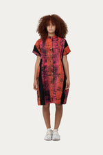 Knee-length Bata Dress in vibrant Carmine batik, with abstract tie-dye pattern and white sneakers.