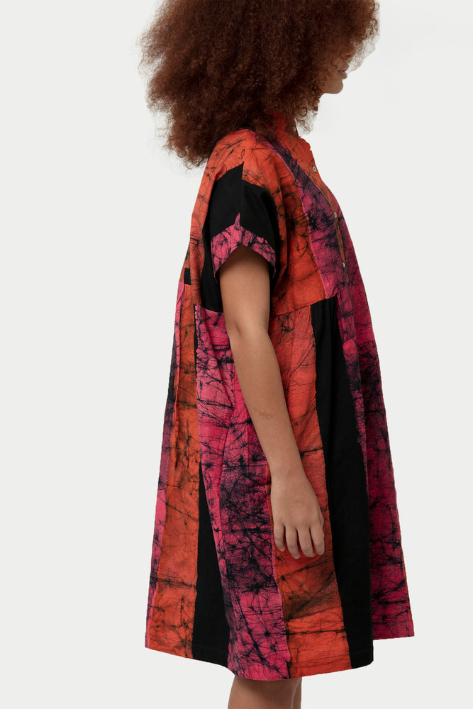 Side profile of Bata Dress in Carmine, highlighting abstract red and pink patterns and black side panels.