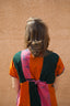 Colorful Bata Dress in Carmine print from behind, tied with a pink ribbon, against a textured wall.