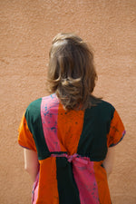 Colorful Bata Dress in Carmine print from behind, tied with a pink ribbon, against a textured wall.