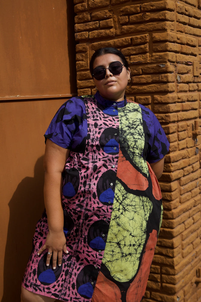 Woman in the size 3 vibrant Bata dress in the colorful Hocus Pocus print poses by brick wall.