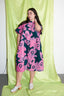 Confident stance in knee-length Bata Dress with pink and navy pattern, paired with white shoes against a green backdrop.