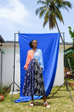Outdoor shot of Bating Dress with half orange and blue top and patterned skirt, in front of a blue backdrop.