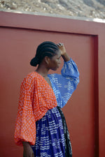 Colorful Bating Dress against a red wall, with braided hair and hand raised in a poised stance.