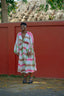 Serene Dreams Bata Dress against a red wall, with a semi-transparent striped robe and dark sandals.