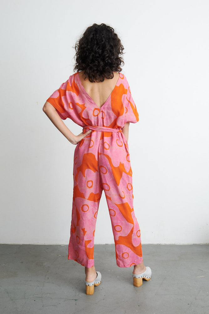 Back view of Easy Jumpsuit in Tee Hee, highlighting the loose fit and open back design, against a white wall.