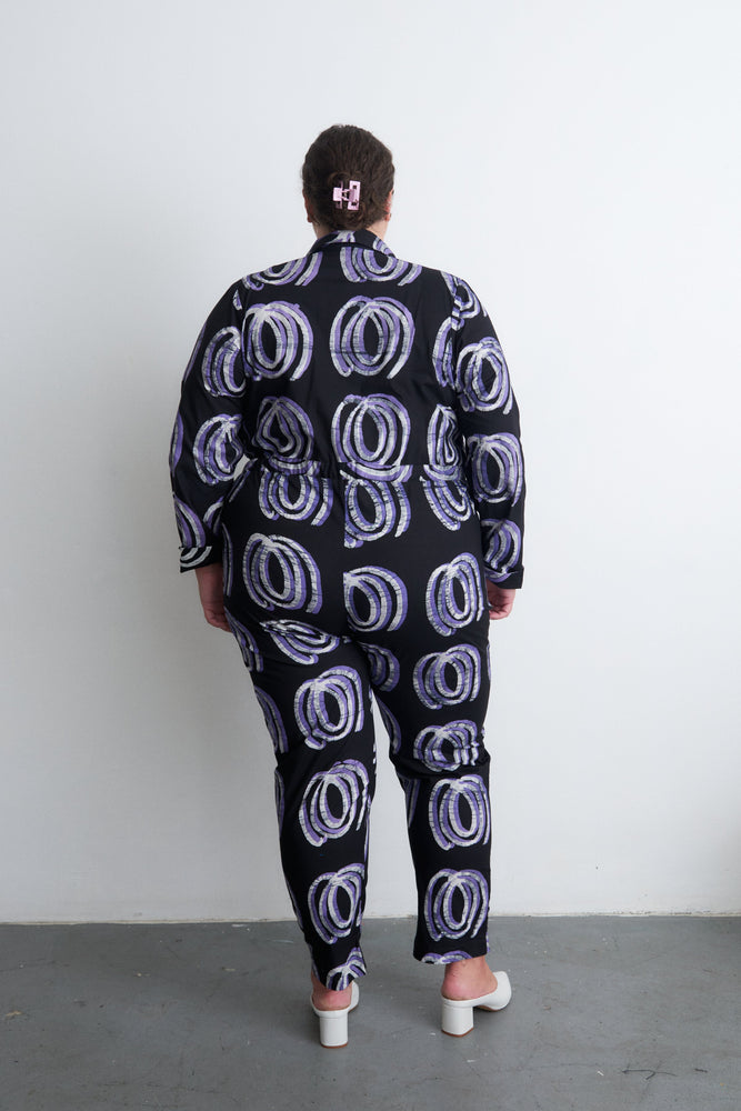 Back view of Accra Jumpsuit in Good Signal print, loose fit with tapered sleeves, against a plain white wall.
