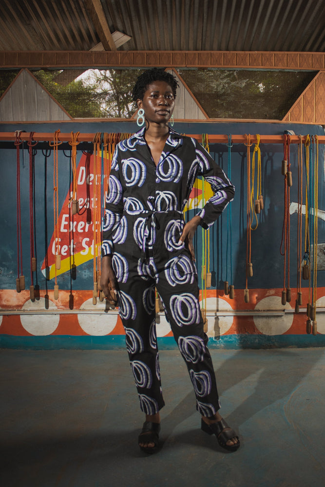 Accra Jumpsuit in Good Signal print, full-sleeve, white circles on dark fabric, colorful abstract mural backdrop.