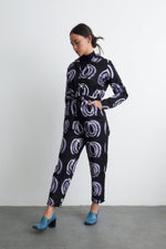 Accra Jumpsuit with Good Signal pattern, full-sleeve design, and blue heels, against a light wall for a sleek look.